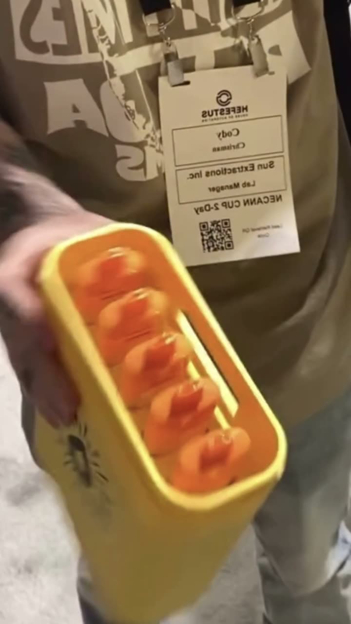 Hands holding the yellow MEGA vape on a show floor, the frame the footage opens on
