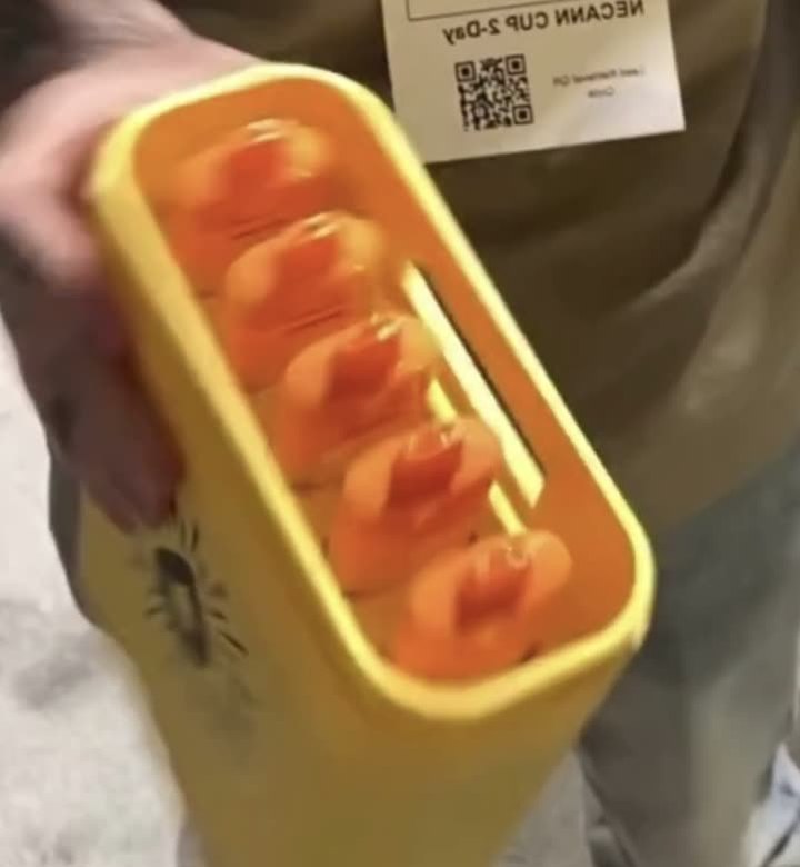 Two hands holding the MEGA vape from above on the show floor, the five orange device tops visible